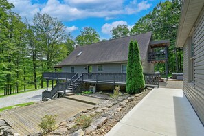 A two-story house with a covered deck, a stone retaining wall, and a gravel driveway. - ‘Shady Point Retreat’ w/ Hot Tub & Pickleball! (Killbuck)