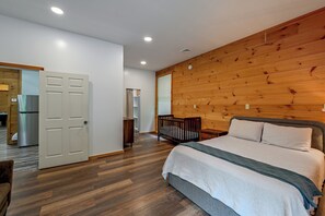 Een slaapkamer met een houten wand, een bed, een ledikant en een deur naar een badkamer.