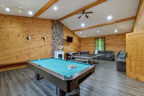A pool table in a room with wooden walls, a stone fireplace, a ceiling fan, and a sofa. - ‘Shady Point Retreat’ w/ Hot Tub & Pickleball! (Killbuck)