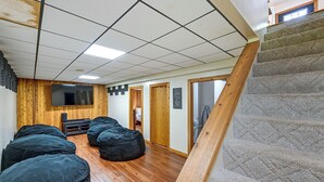 A room with a wooden floor, a flat-screen TV mounted on the wall, and a staircase with a wooden handrail.