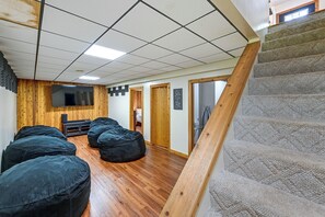 A room with a wooden floor, a flat-screen TV mounted on the wall, and a staircase with a wooden handrail. - ‘Shady Point Retreat’ w/ Hot Tub & Pickleball! (Killbuck)
