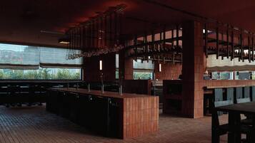Een restaurantinterieur met bakstenen vloer, houten tafels en banken, hangende lampen en grote ramen.