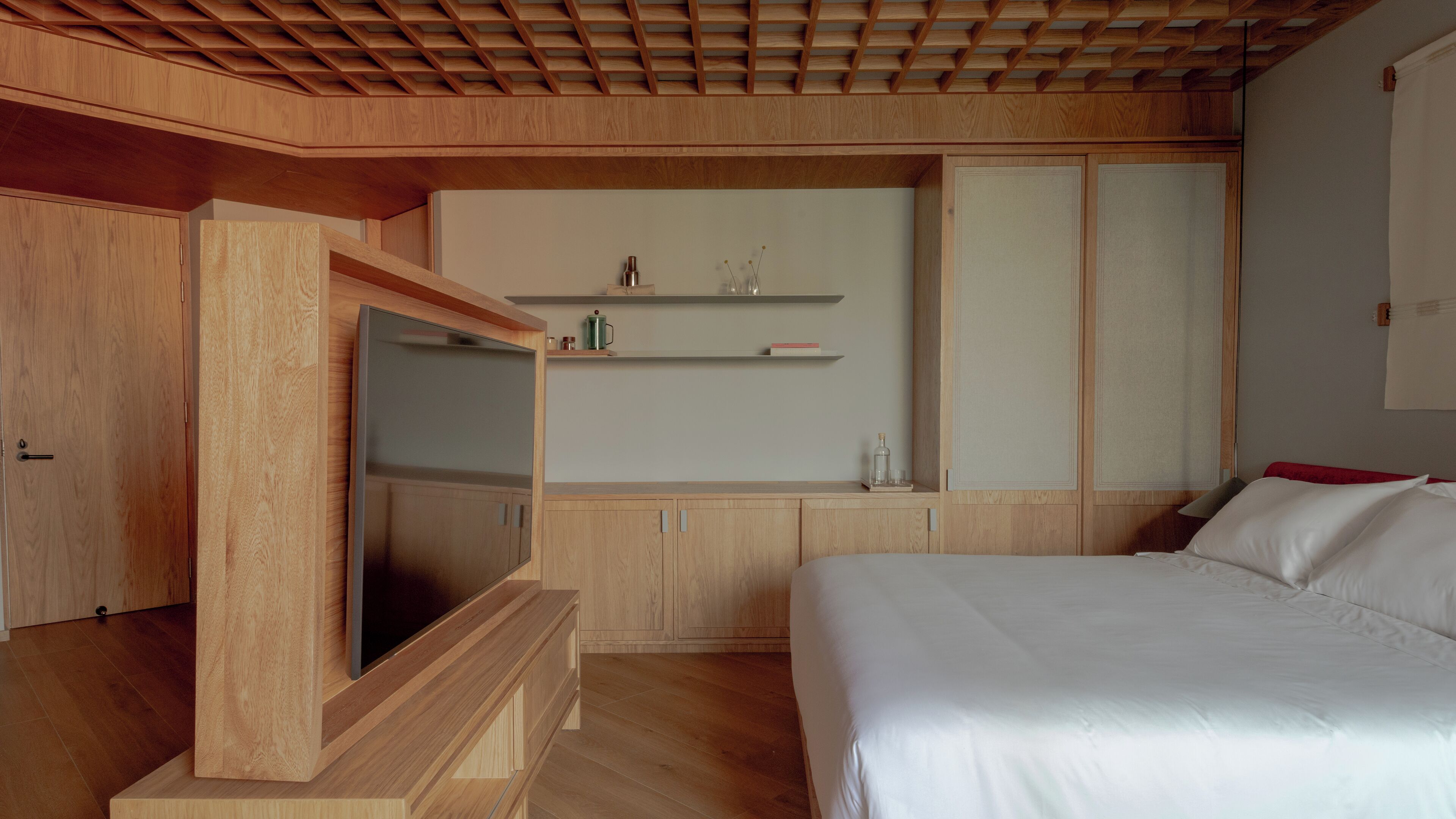 A modern bedroom with a wooden ceiling, built-in TV, and a bed with white bedding.