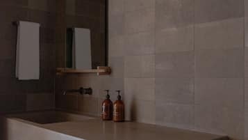 A modern bathroom with a large bathtub, a mirror, and a shelf with toiletries.