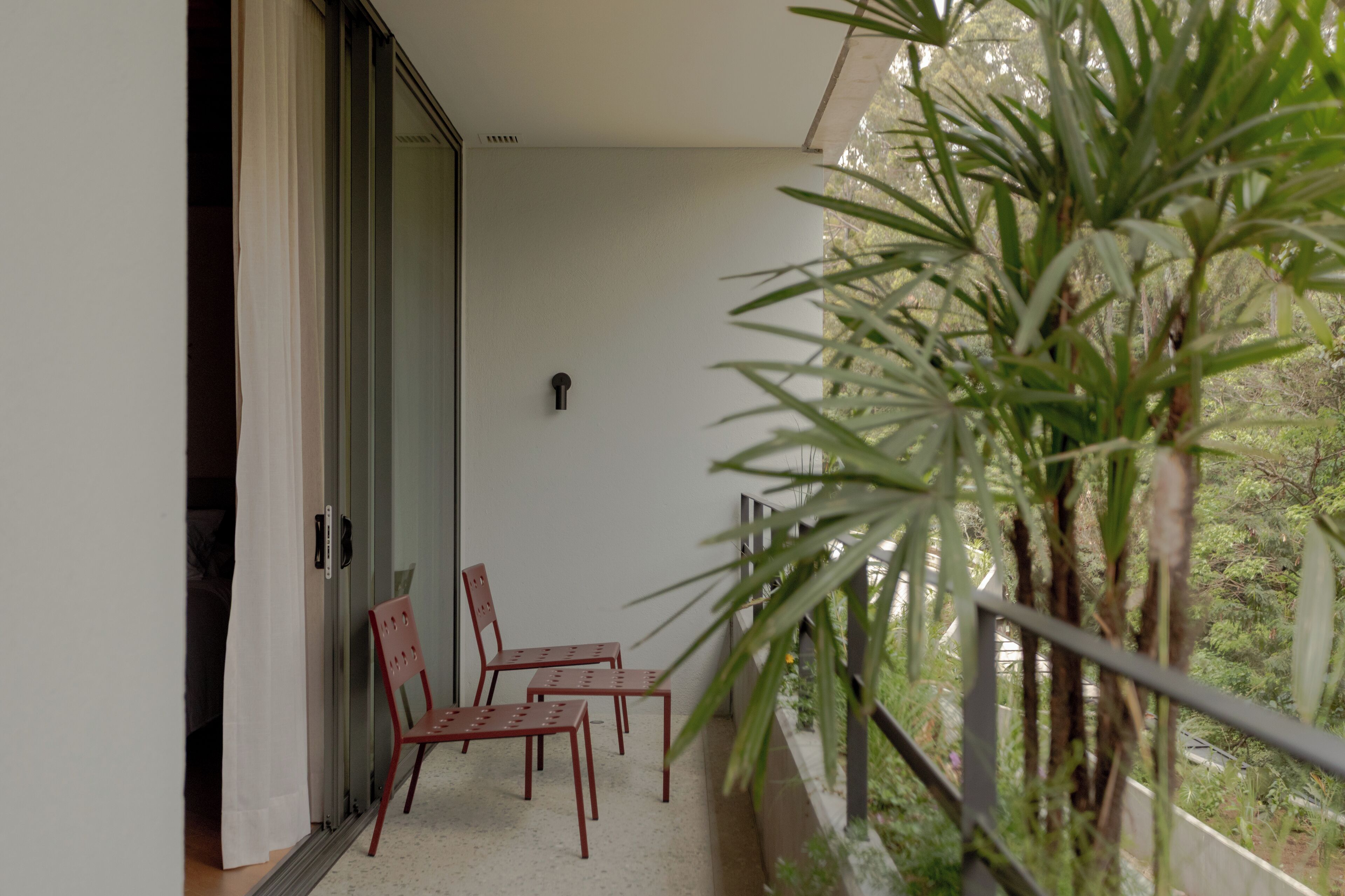 A balcony with two red chairs, a glass door, and a potted plant.