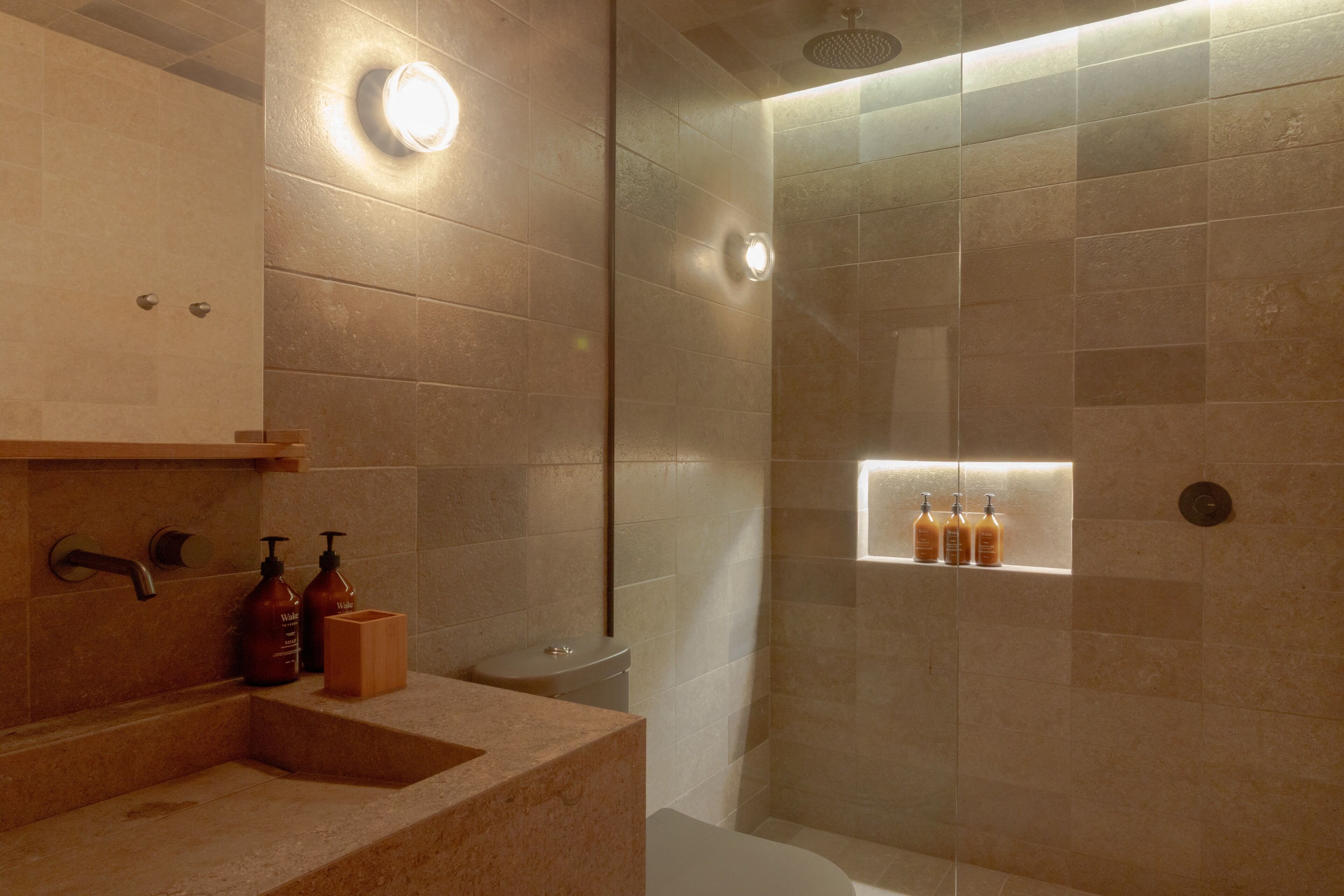 A modern bathroom with a glass-enclosed shower, a vanity with a sink, and a shelf with toiletries.