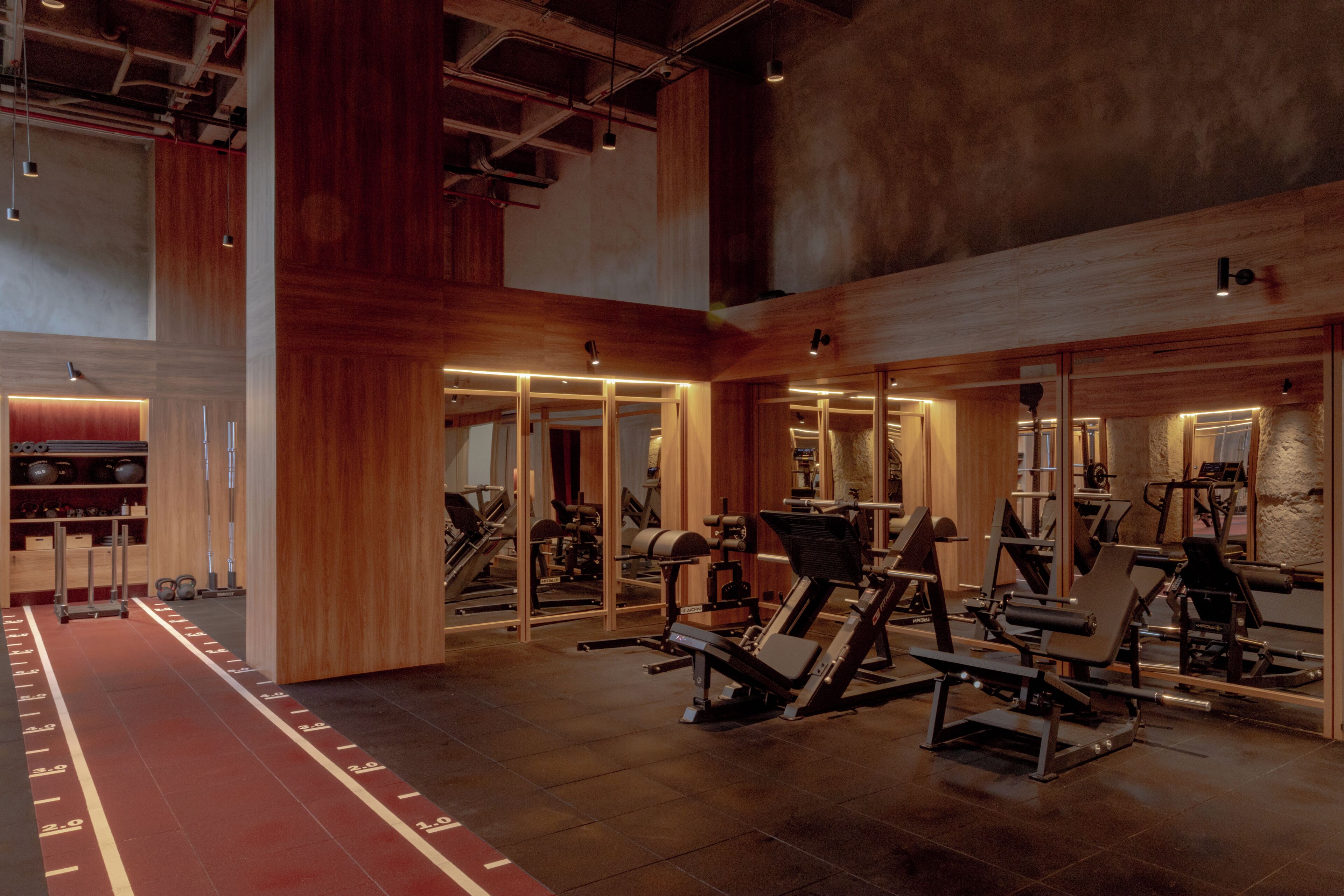 Een sportschool met diverse fitnessapparaten, houten wanden en een rode loopbaan.