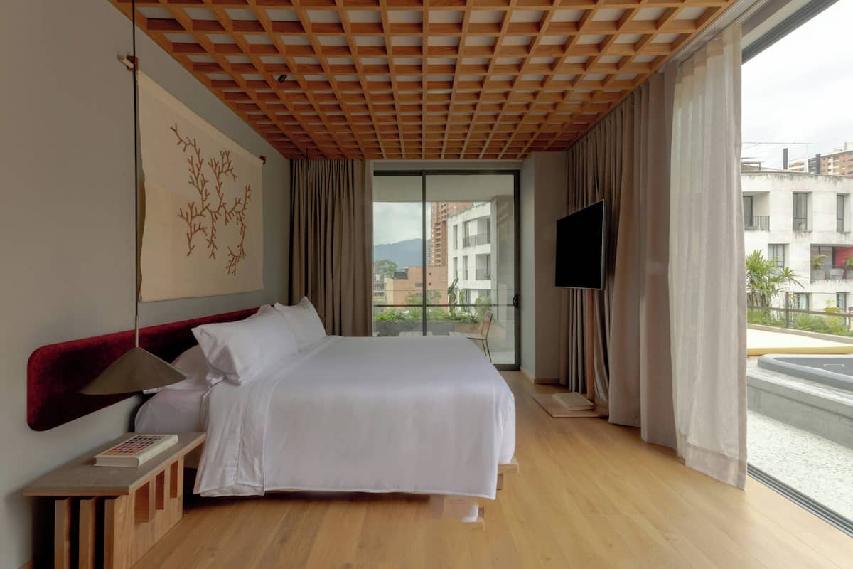 A modern hotel room with a large bed, a TV, and a view of the city.