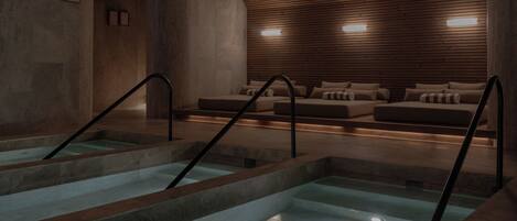 Un espacio de spa con piscina, paneles de madera y una zona de estar con cojines.