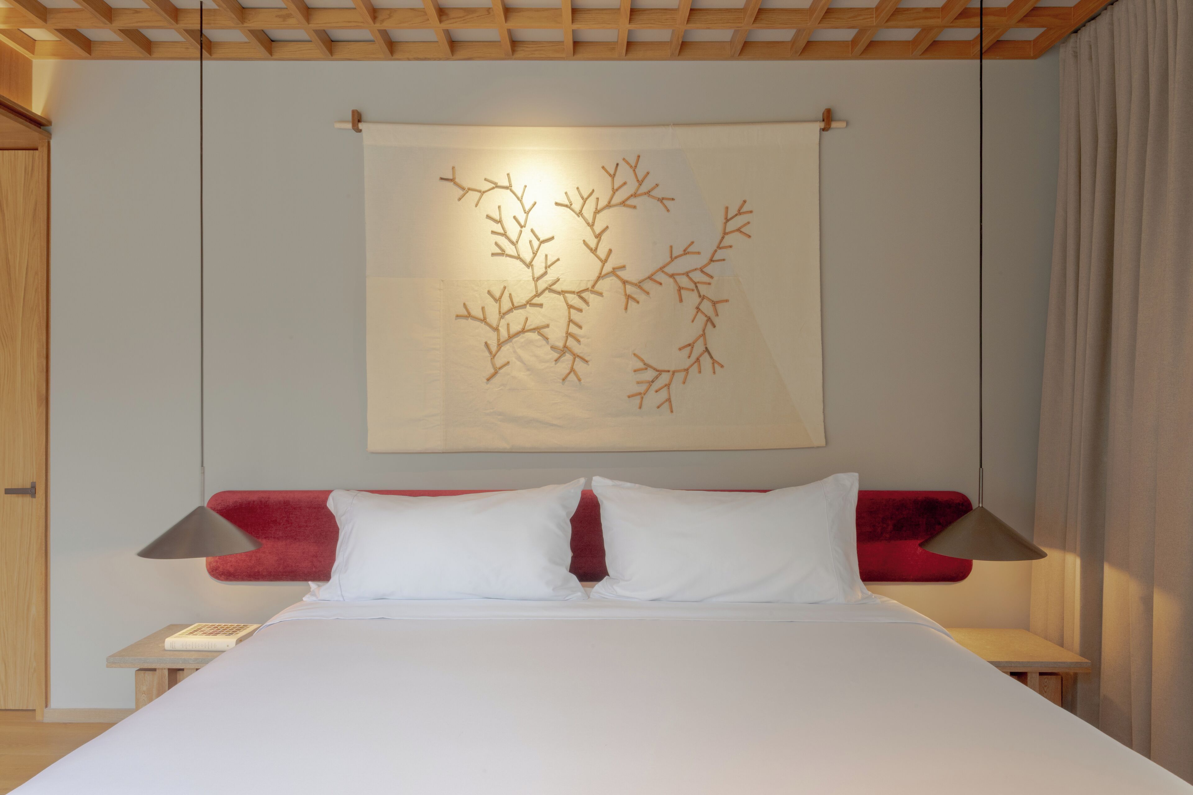 A neatly made bed with white linens, a red headboard, and a wall-mounted artwork.