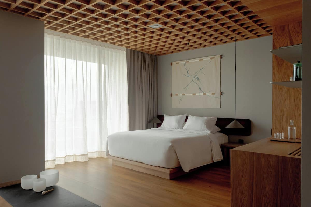 A modern hotel room with a wooden ceiling, a large bed, a bedside table, and a wall-mounted artwork.