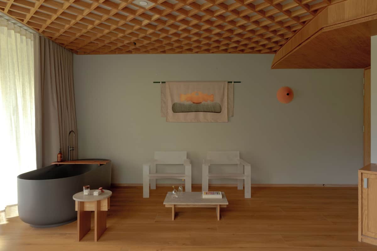 A modern living room with a large bathtub, two white chairs, a small table, and a wooden ceiling.