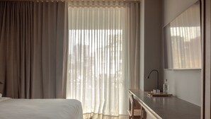 A hotel room with a wooden ceiling, a bed, a desk with a mirror, and a window with curtains. - Wake Medellin, a Member of Design Hotels (Medellín)