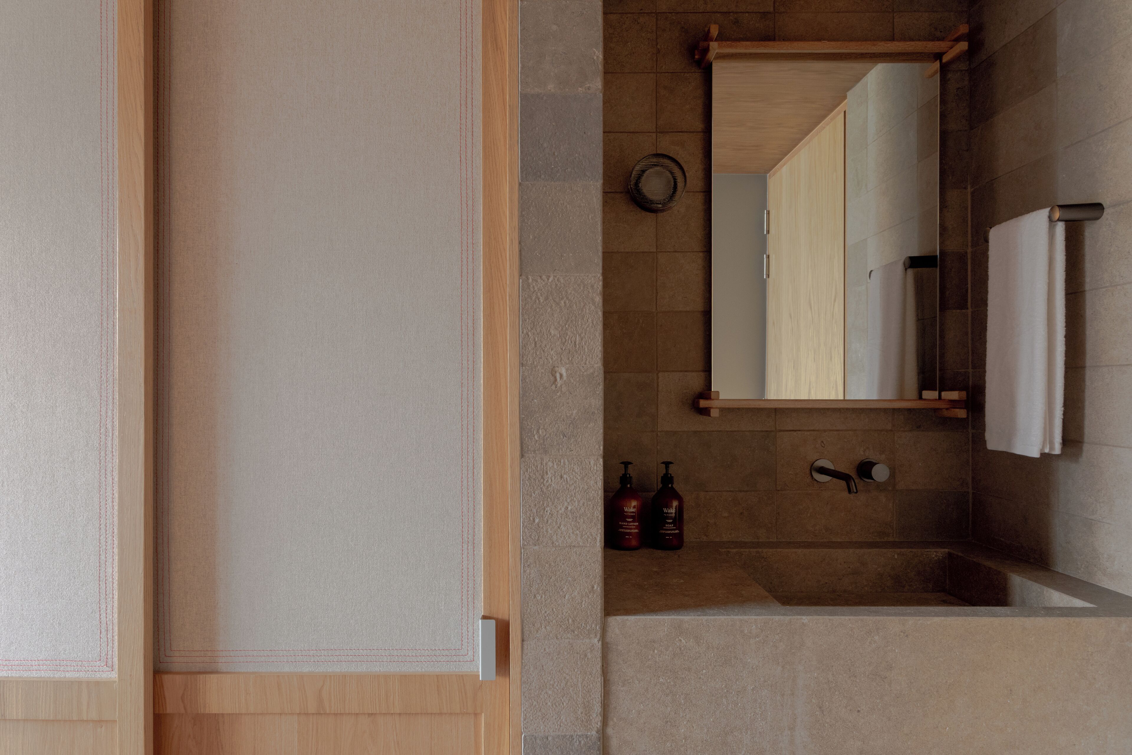 Ein Badezimmer mit Holztür, Spiegel, Waschbecken und zwei Shampoo-Flaschen.