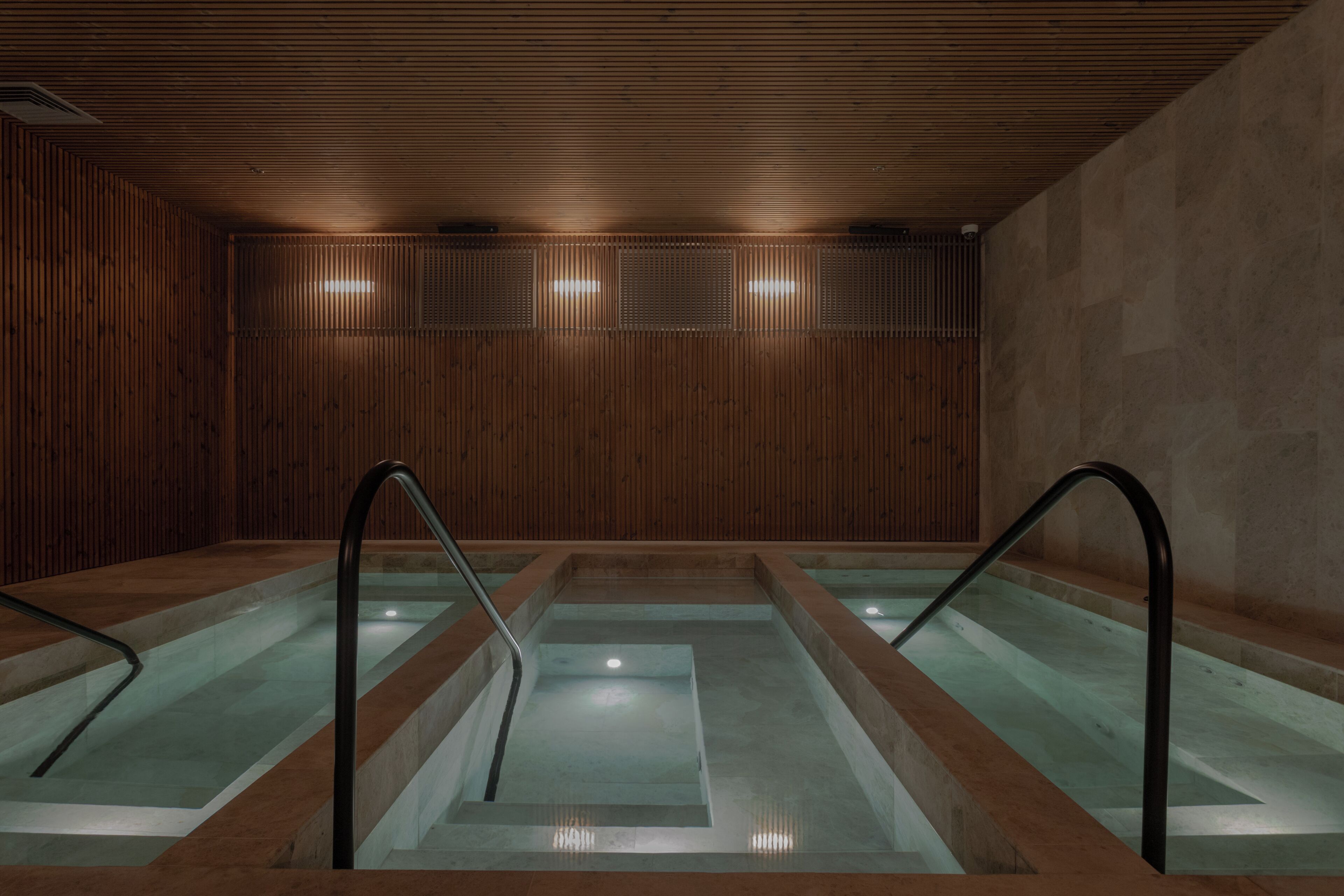 Un área de spa con tres piscinas rectangulares, paneles de madera en las paredes y suelo de baldosas.