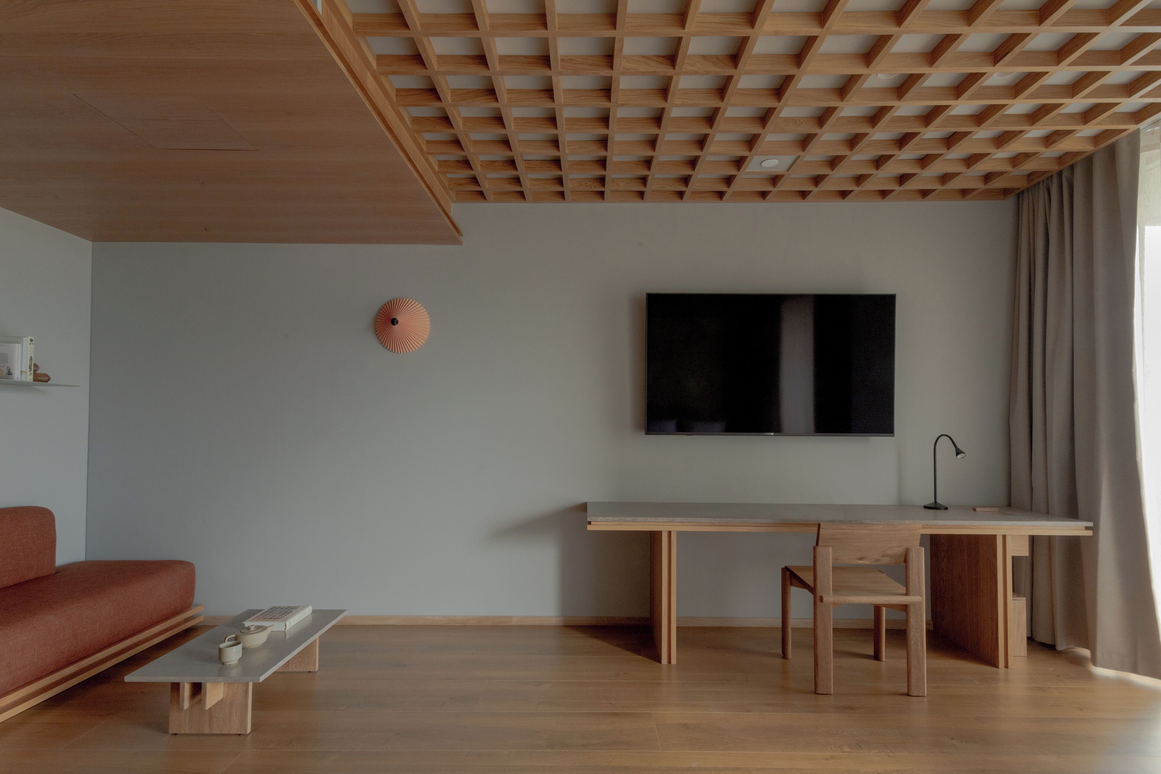 Una sala de estar moderna con techo de madera, un televisor de pantalla plana grande, un escritorio, una silla y un sofá.