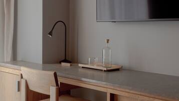 Habitación minimalista con un escritorio de madera, una silla, una lámpara y un televisor de pantalla plana en la pared.