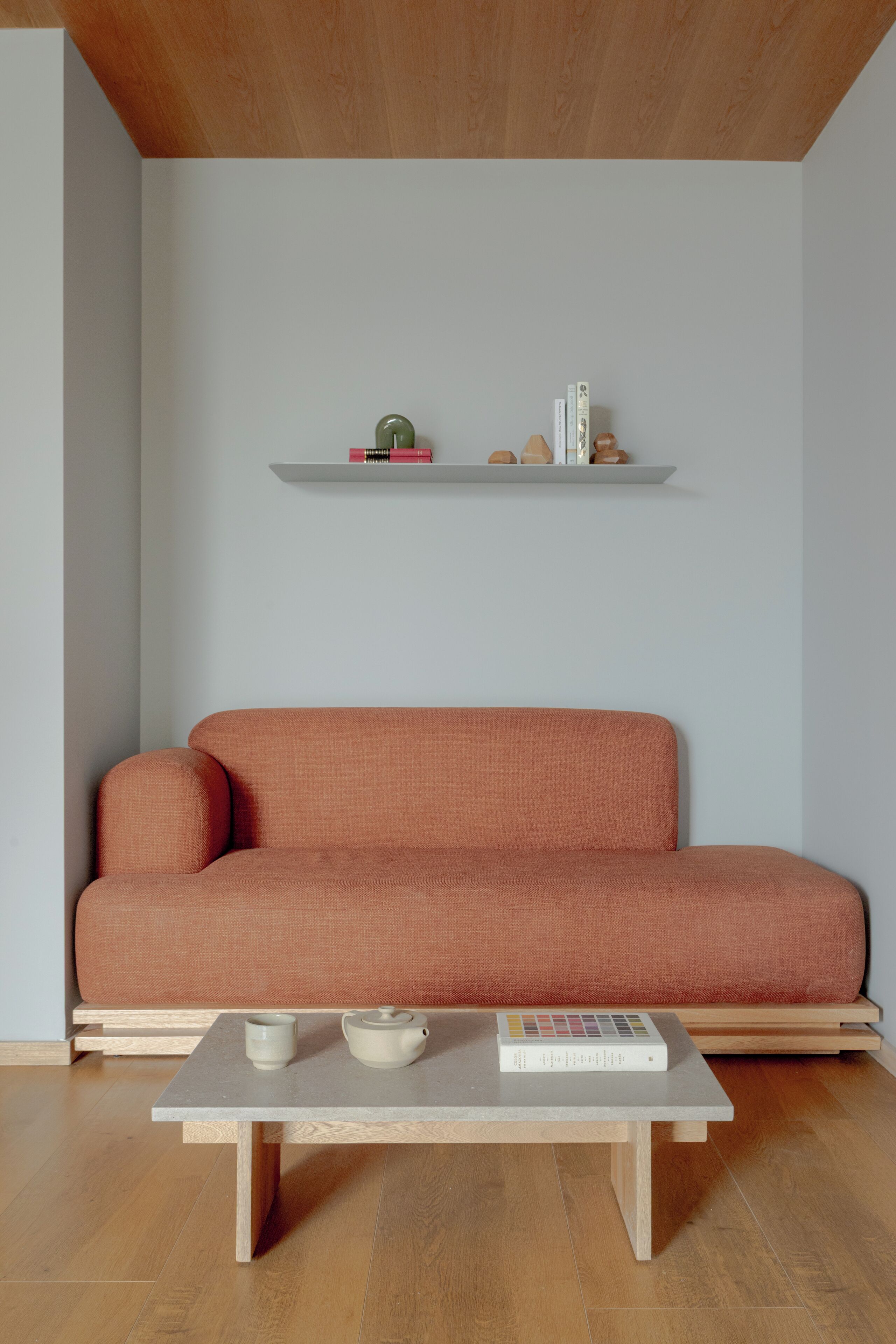 A minimalist living room with a sofa, a coffee table, and a shelf with books and decorative items.