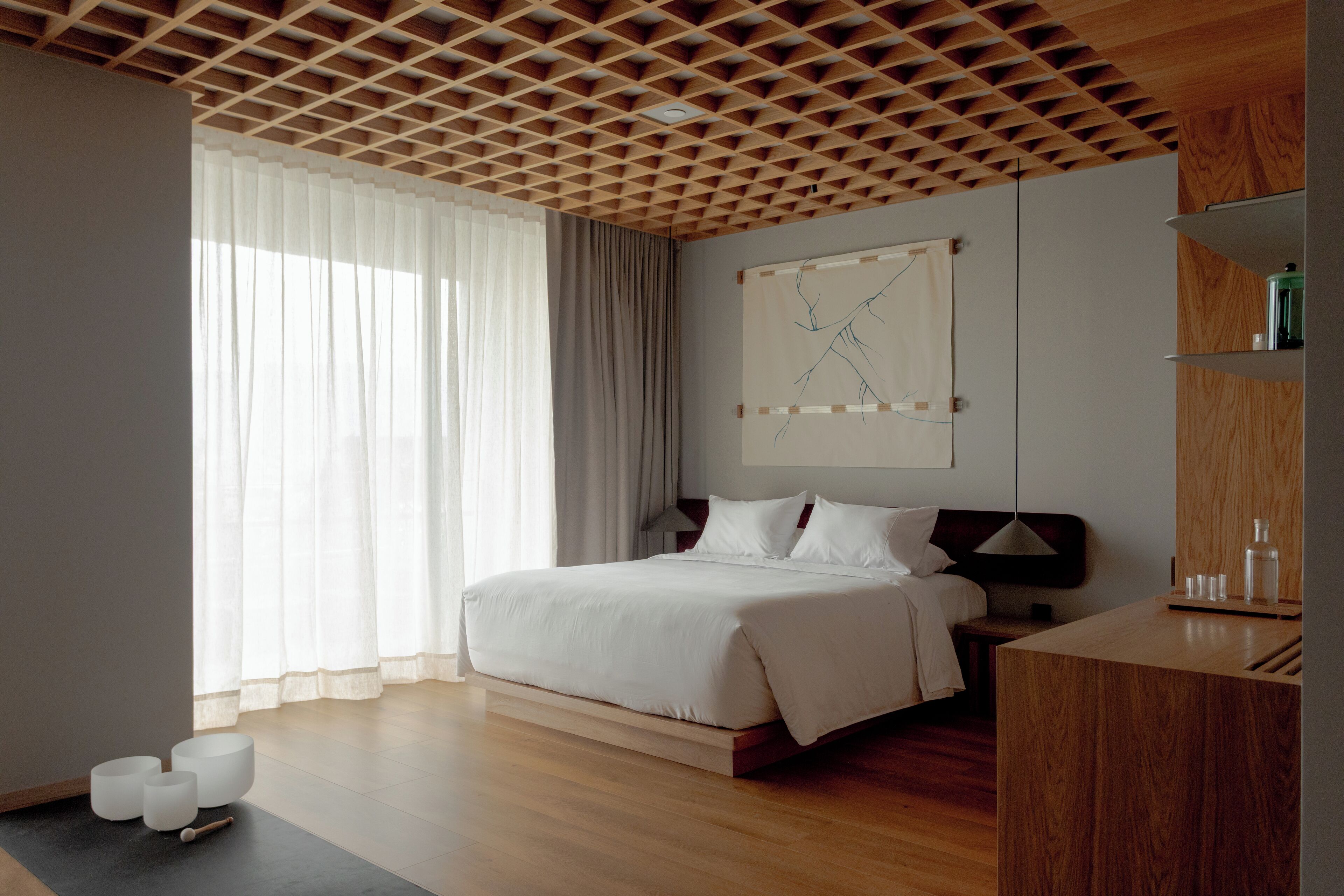 A modern hotel room with a wooden ceiling, a large bed, a bedside table, and a wall-mounted artwork.