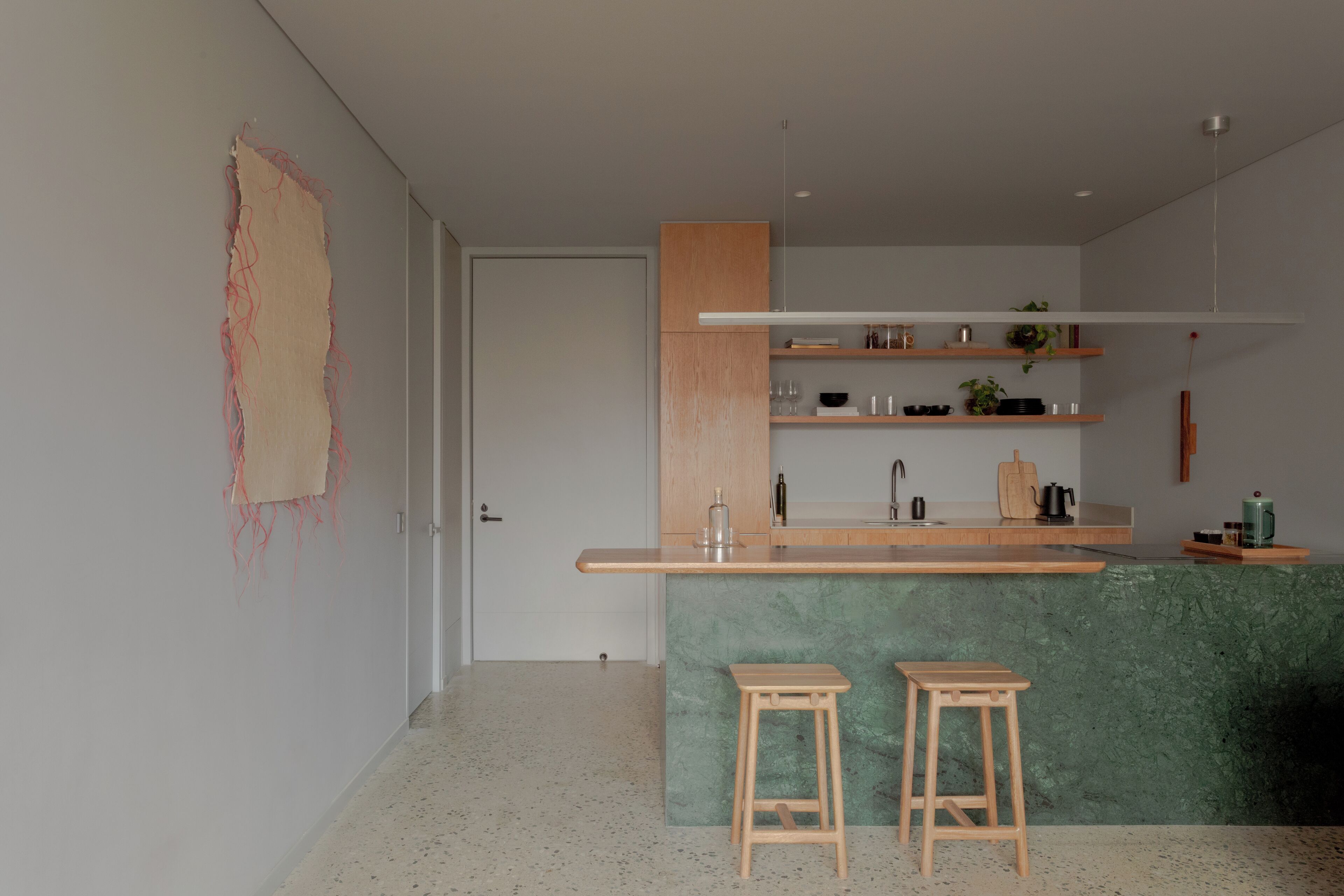 Een moderne keuken met een groen aanrecht, houten krukken en een minimalistisch ontwerp.