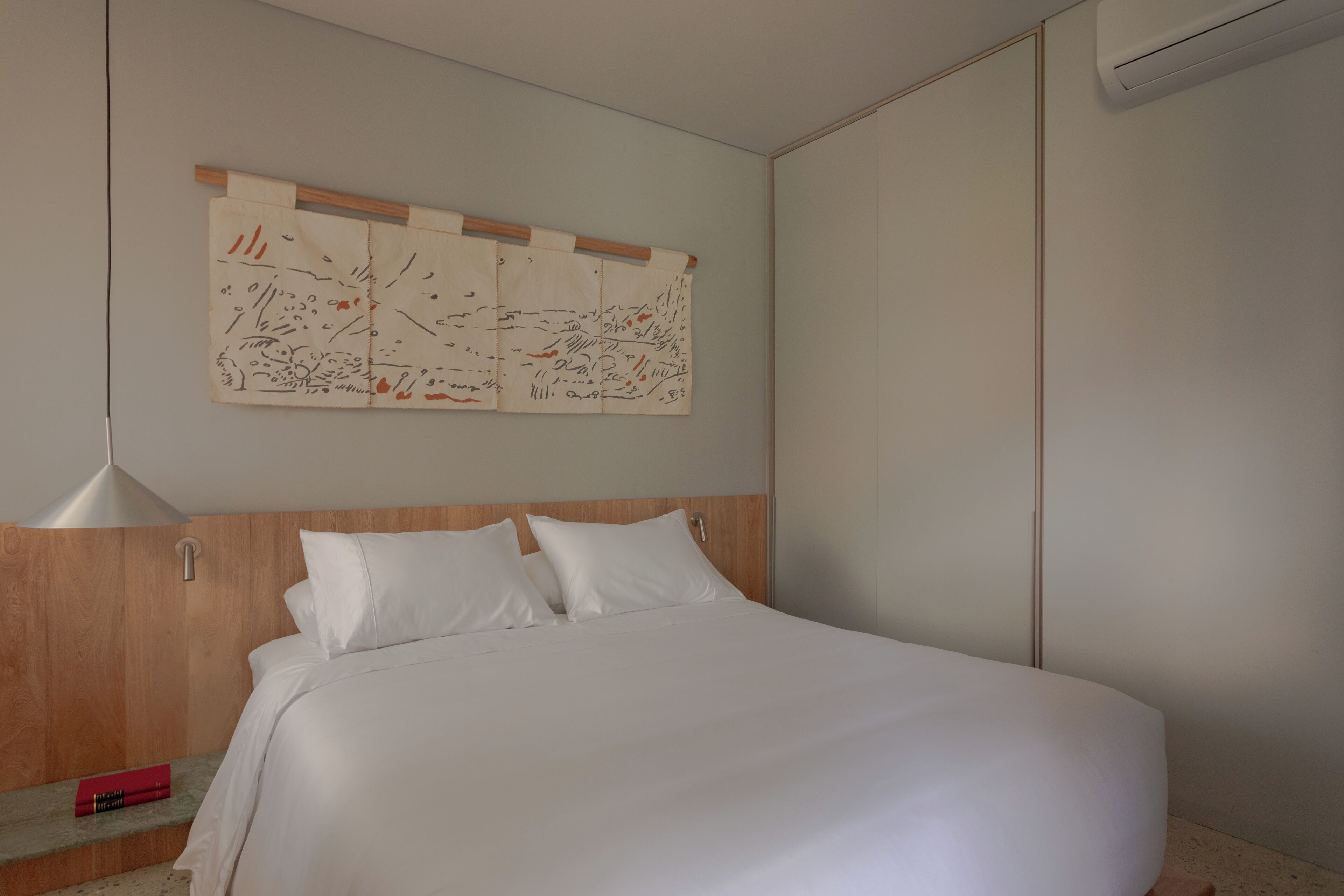 A neatly made bed with white linens, a wooden headboard, and a wall-mounted artwork.