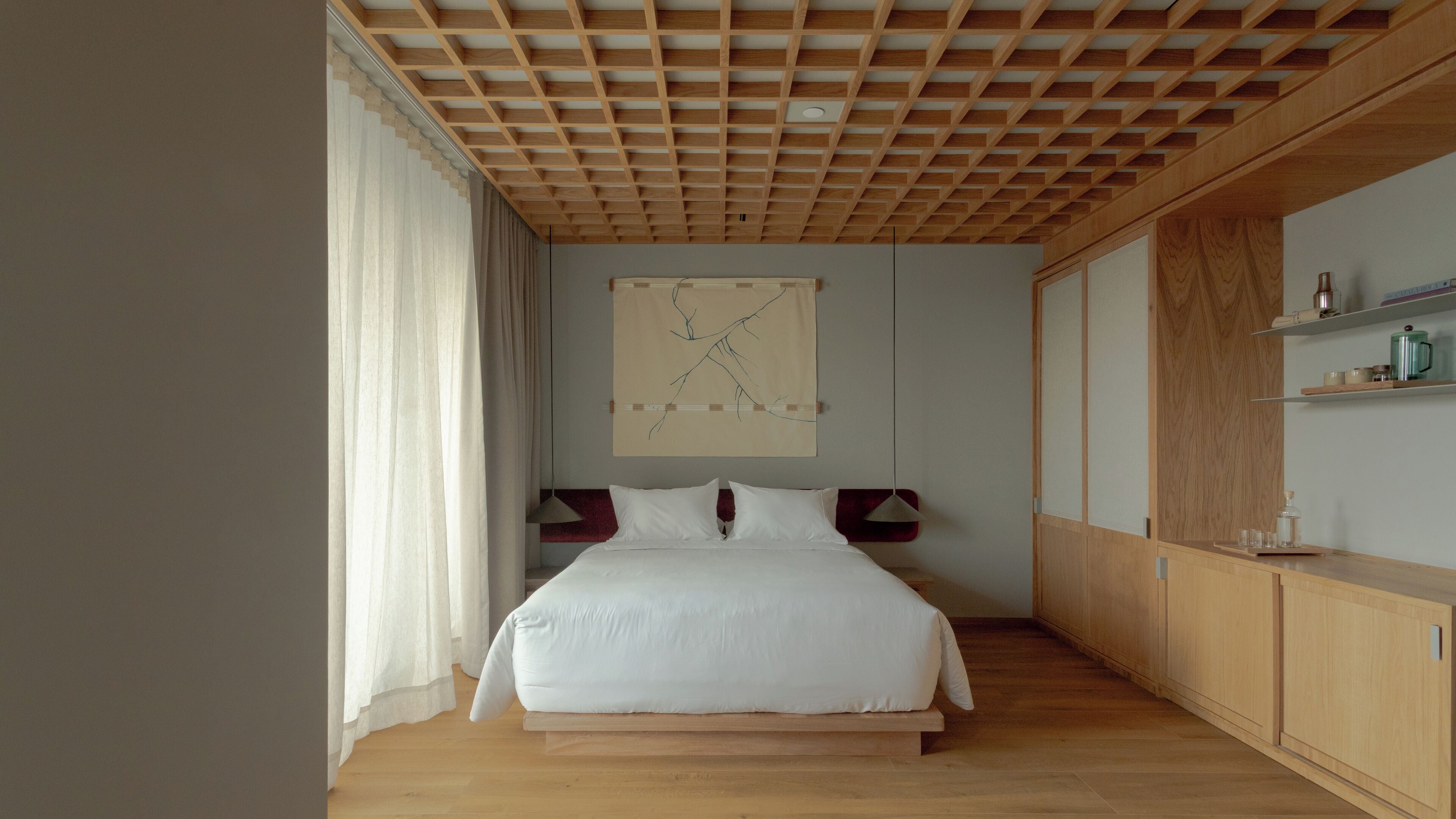 Un dormitorio moderno con techo de madera, una cama grande, una obra de arte colgada en la pared y armarios empotrados de madera.