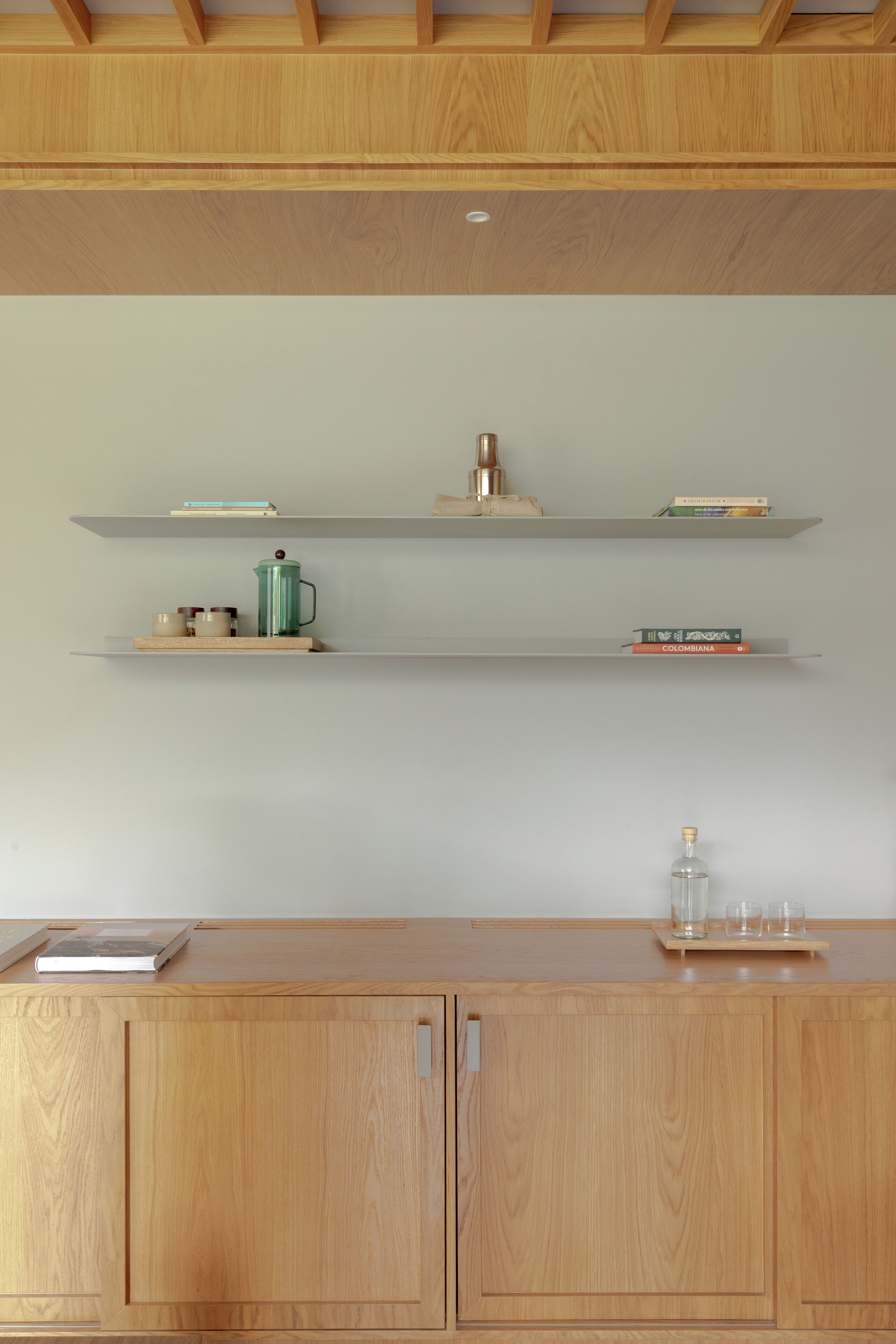 A kitchen with wooden cabinets and shelves holding books and kitchenware.