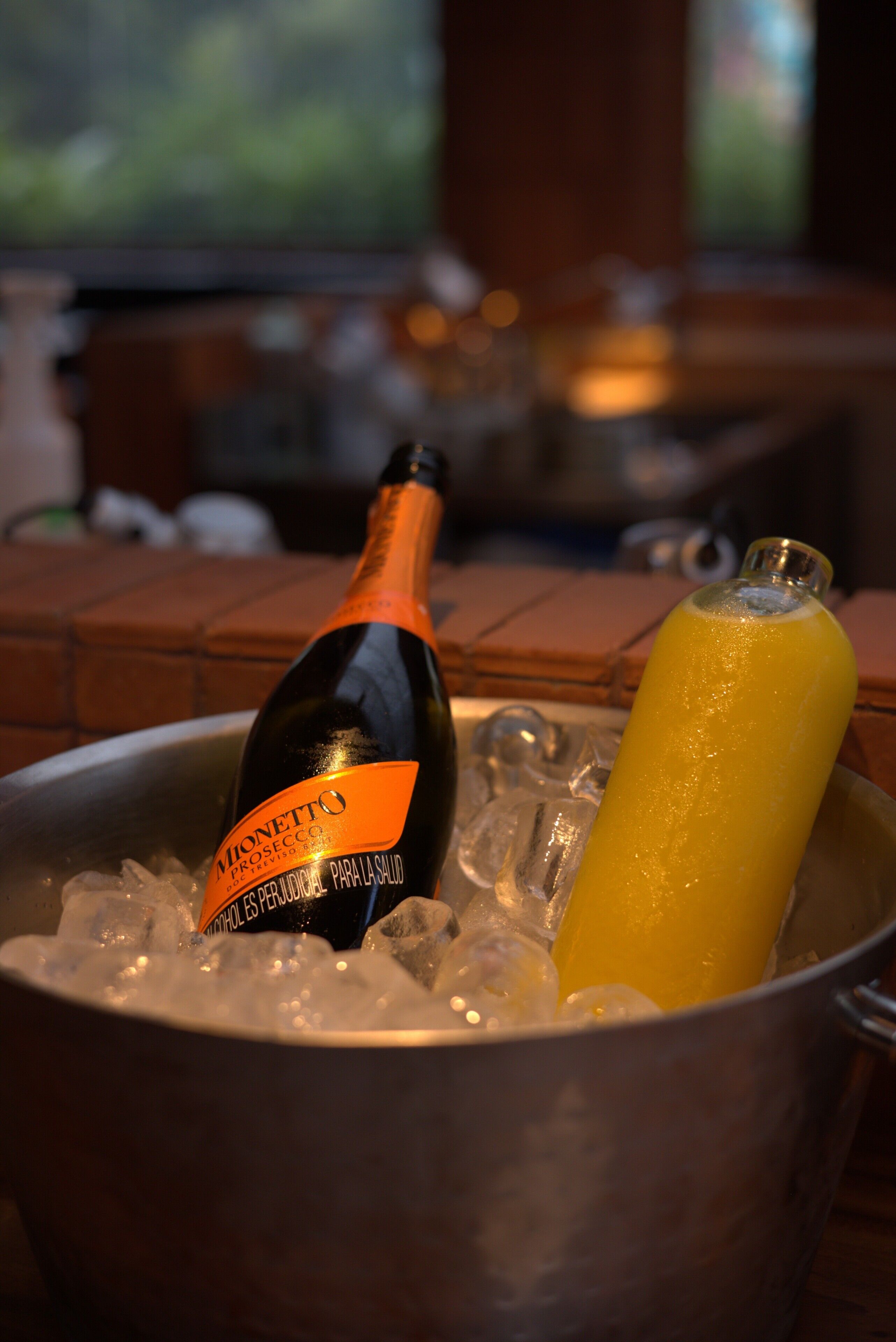 A bottle of Monetto Prosecco and a yellow drink in a metal bucket with ice.