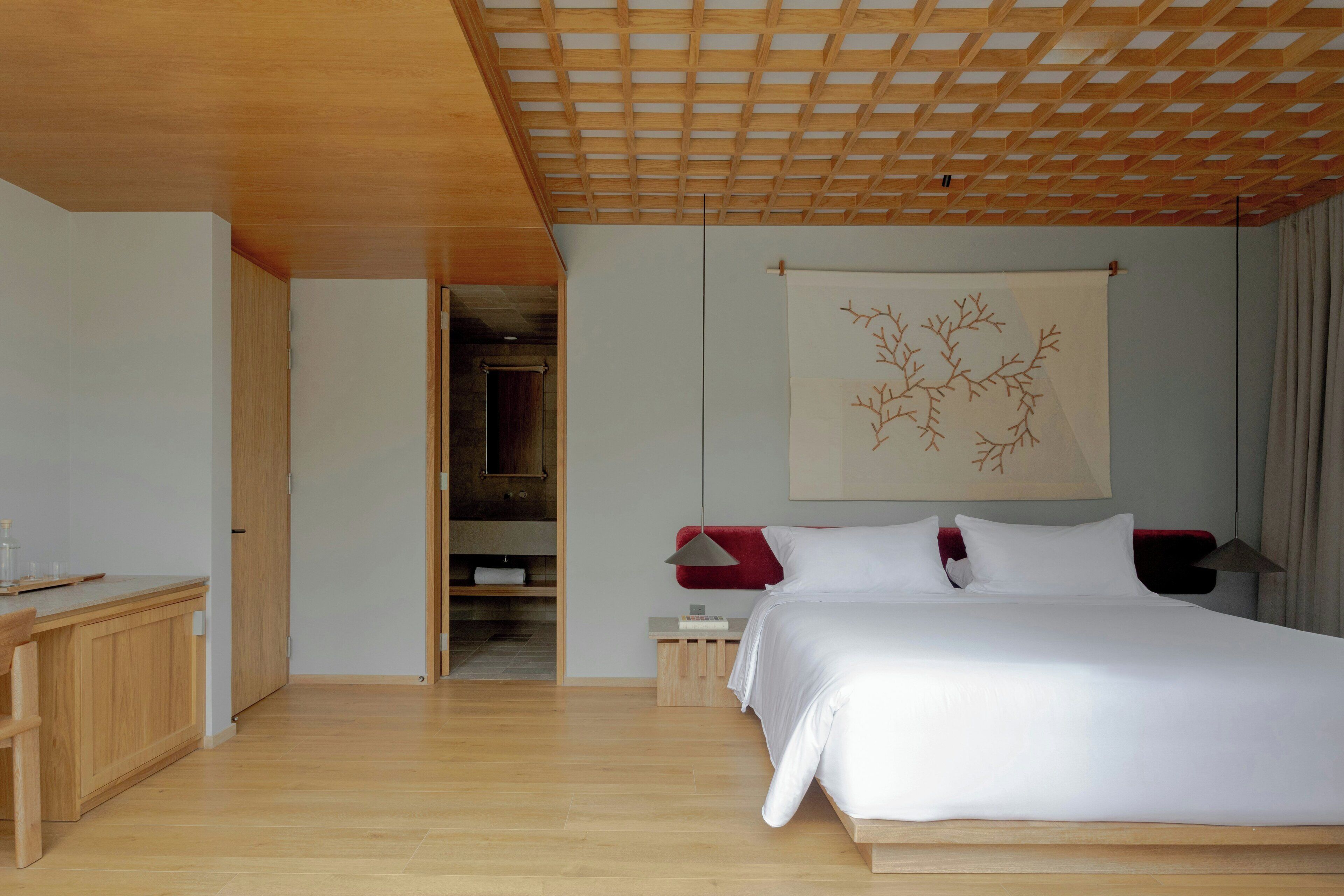 Une chambre avec un plafond en bois, un lit, une table de chevet, une chaise rouge et une armoire.