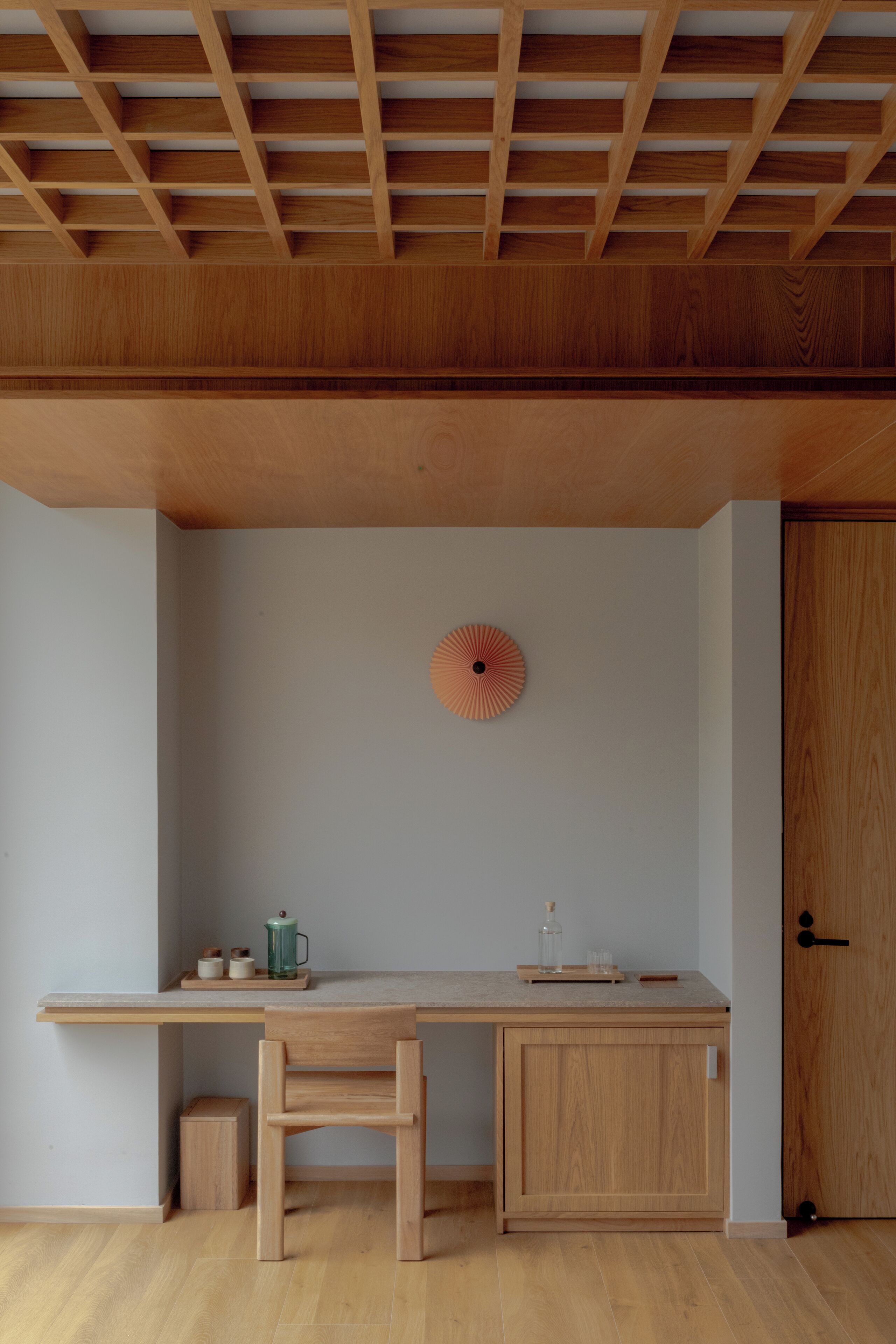 A minimalist room with a wooden desk, a chair, a cabinet, and a wall-mounted decorative item.