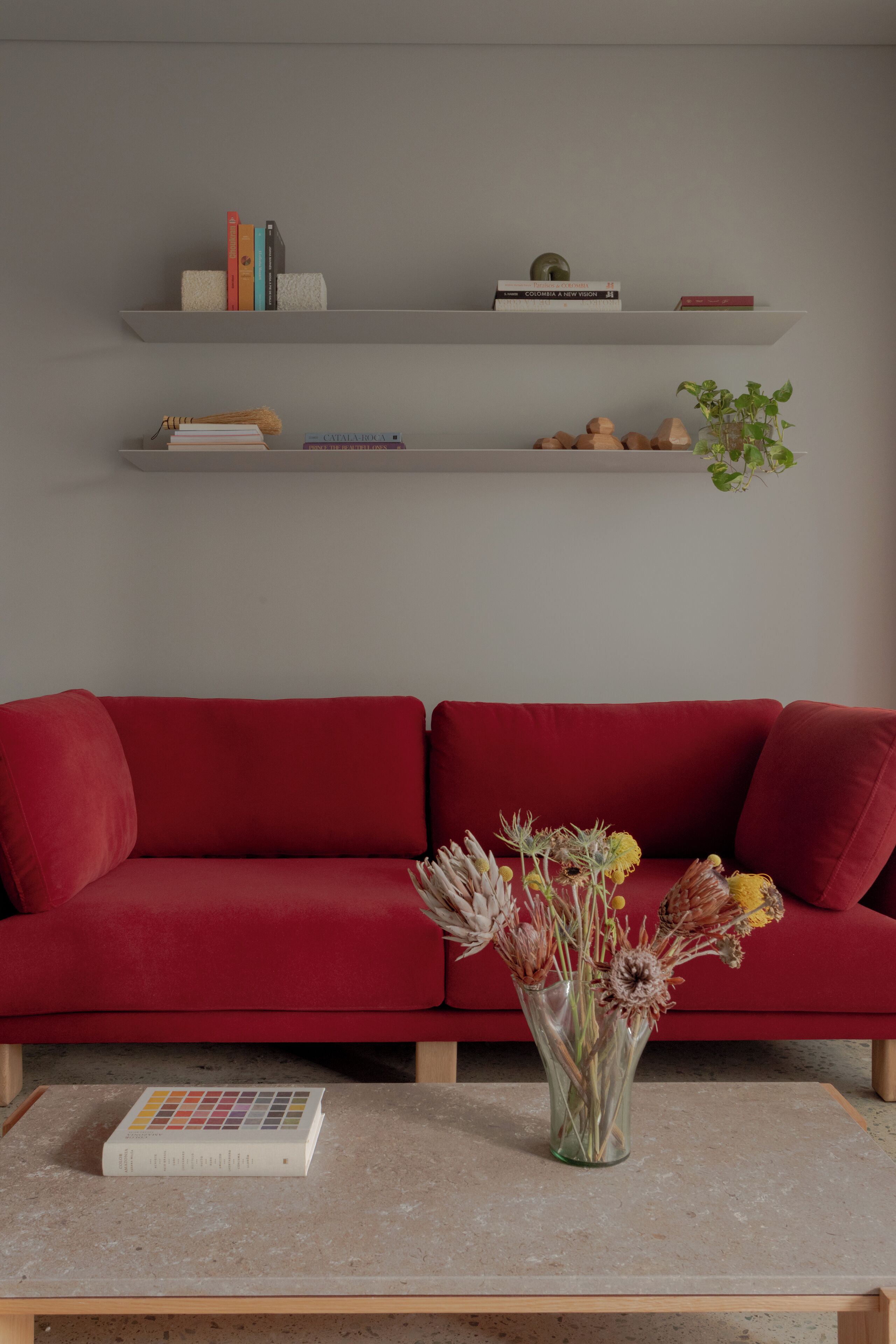 A red sofa with a vase of dried flowers on a table in front.