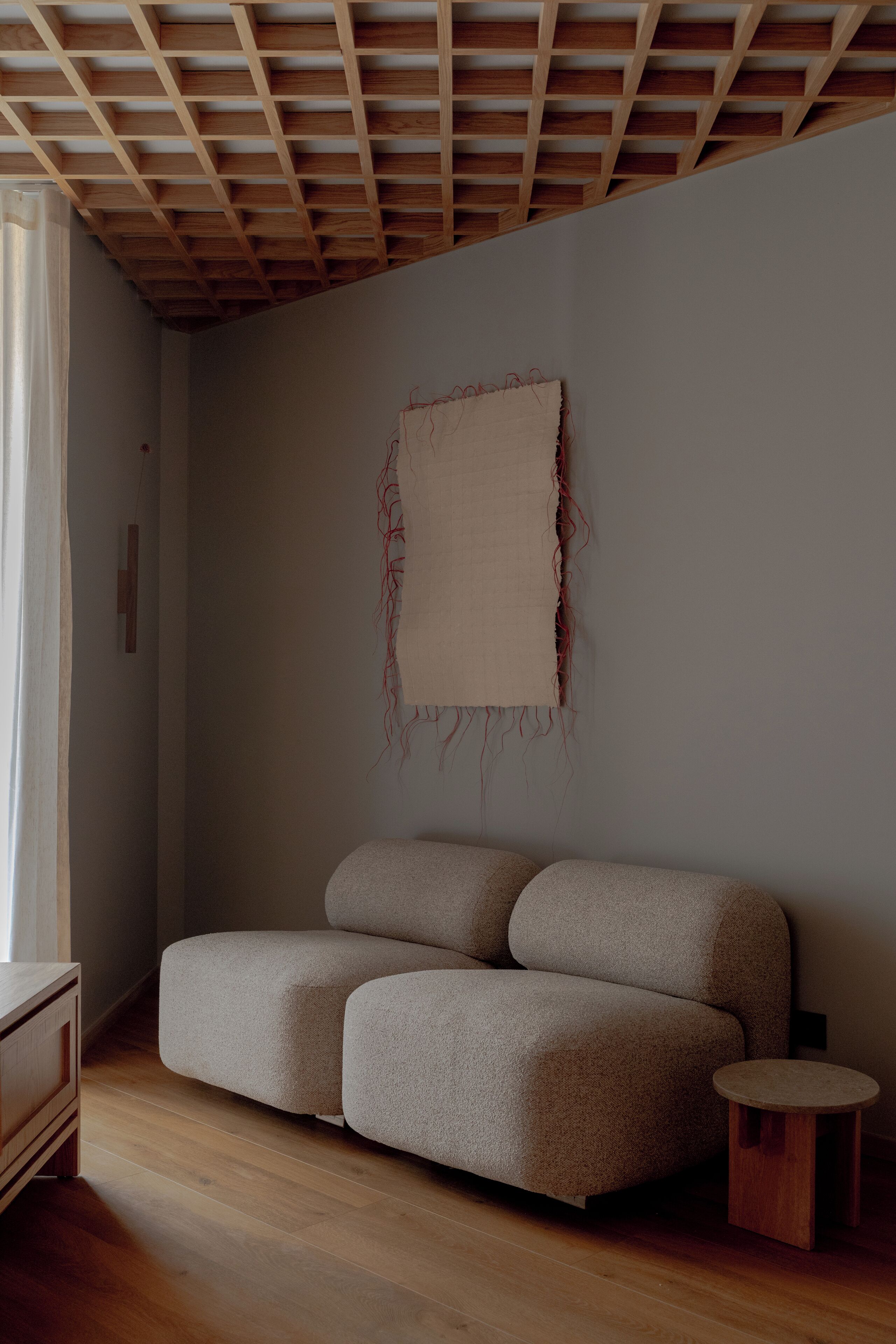 Una habitación con techo de madera, un sofá color beige, una pequeña mesa de madera y un tapiz colgado en la pared.