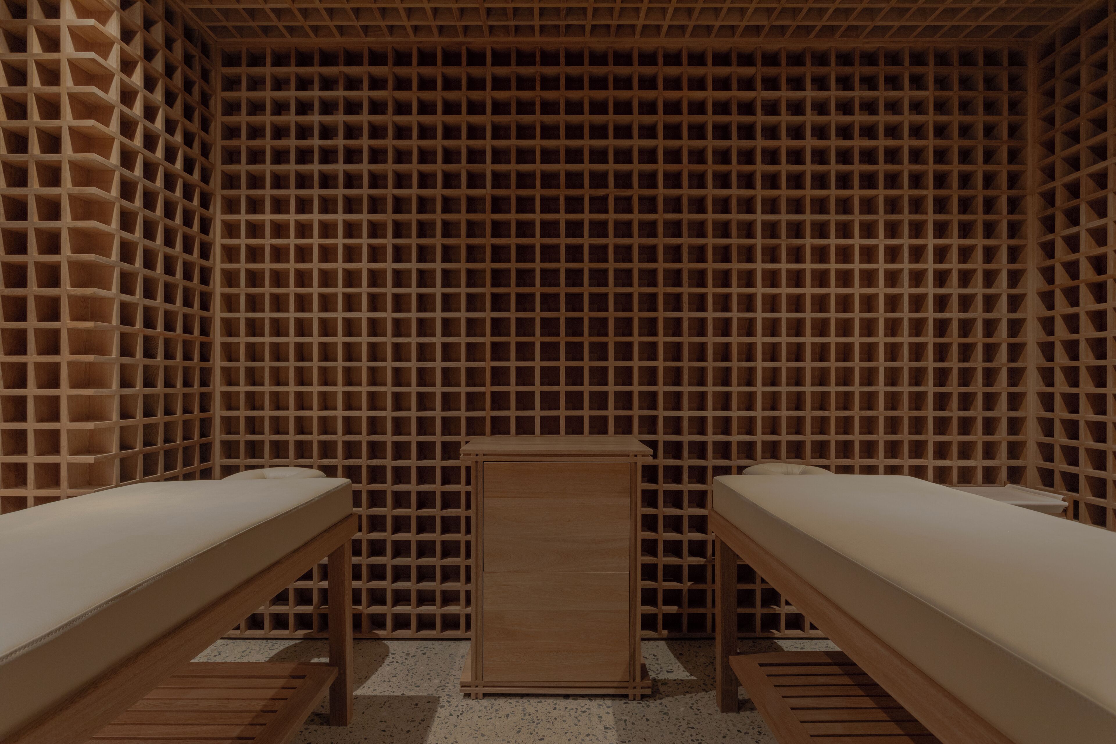 Una habitación con dos camas de madera, un mueble de madera en el centro y un papel tapiz con diseño de cuadrícula.