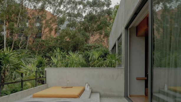 A modern outdoor hot tub area with a concrete wall, a wooden bench, and a glass door leading to a room. - Wake Medellin, a Member of Design Hotels (Medellín)