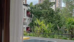 A view from a window of a room with a concrete hot tub, a wooden floor, and a view of a cityscape with buildings and trees. - Wake Medellin, a Member of Design Hotels (Medellín)