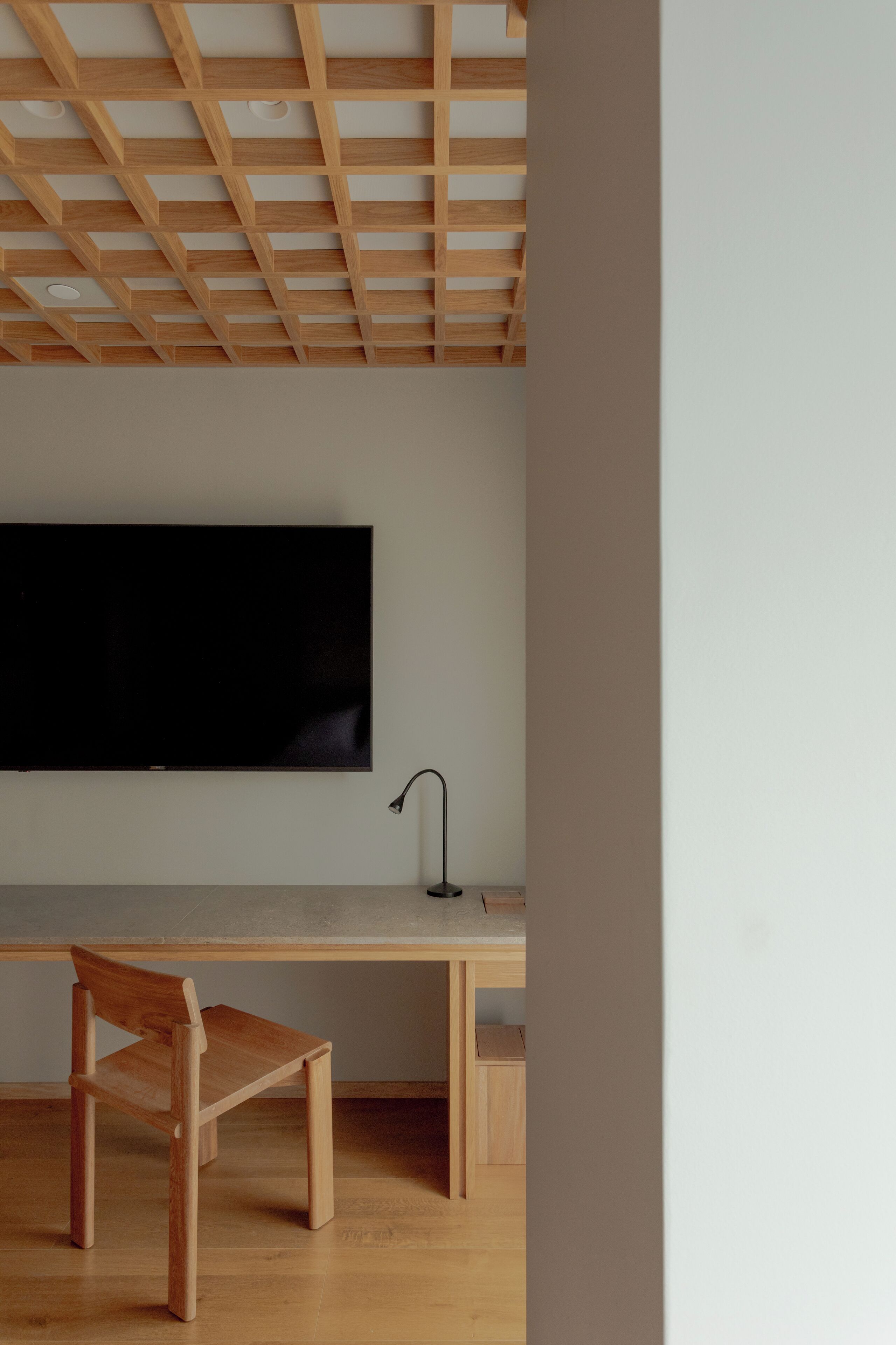 A modern room with a wooden ceiling, a flat-screen TV mounted on the wall, a wooden desk, and a chair.