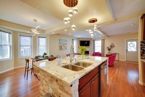 A spacious kitchen with a marble countertop, double sink, and a large island. There are pendant lights hanging from the ceiling and a flat-screen TV mounted above the island. - Walk to Kinnickinnic Ave! Newly Updated Abode (Milwaukee)