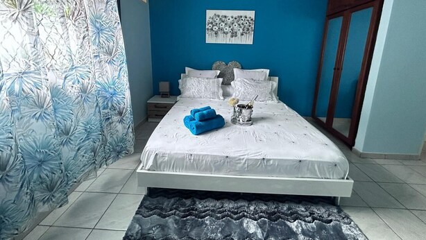 Ein Schlafzimmer mit einem Bett, einem Nachttisch, einer Wand-Klimaanlage und einem Fenster mit Vorhang.