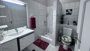 Ein modernes Badezimmer mit Waschbecken, Spiegel und Toilette. Ein Duschbereich mit gefliestem Boden und einer roten Badmatte.