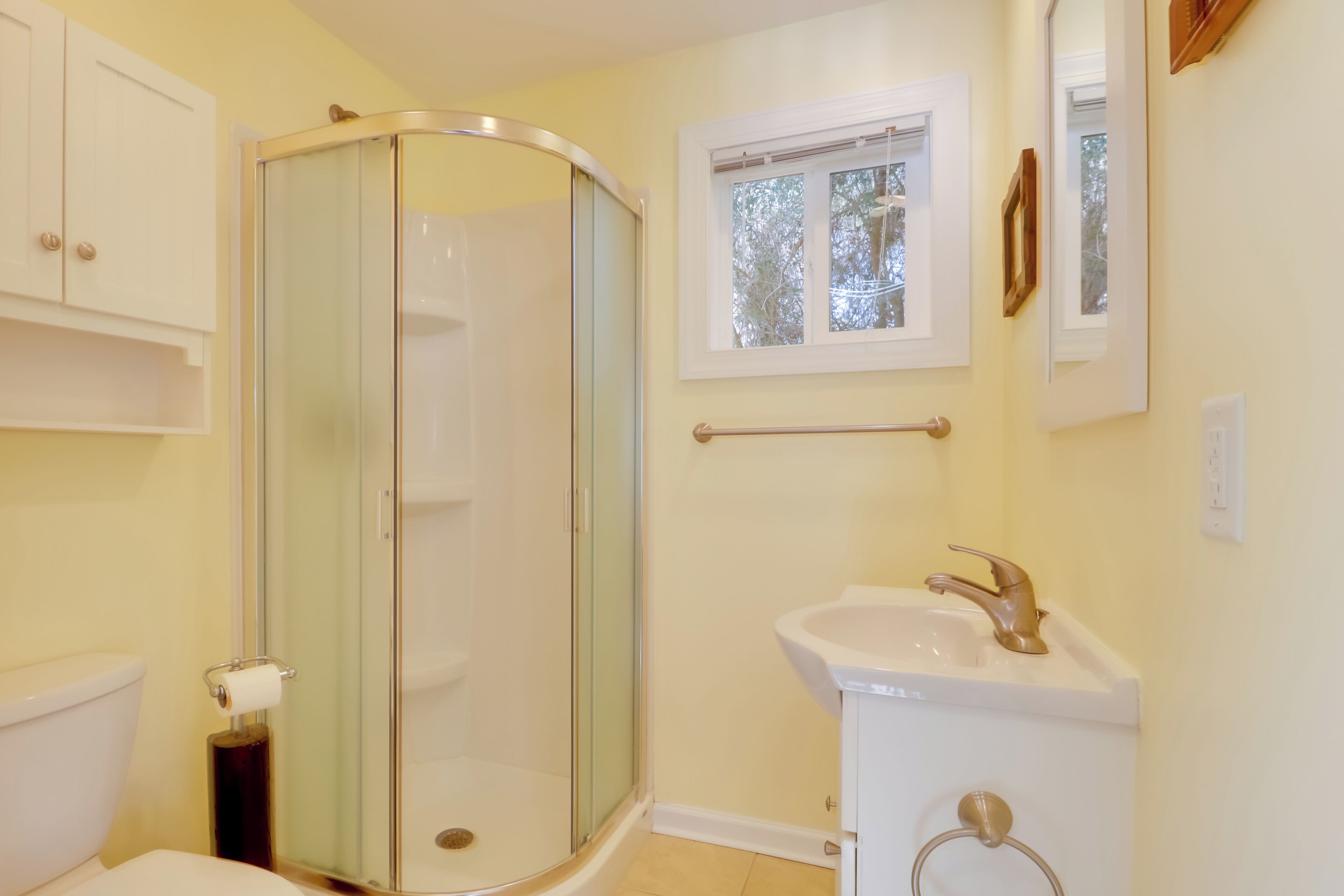 A bathroom with a glass-enclosed shower, a sink, and a window.