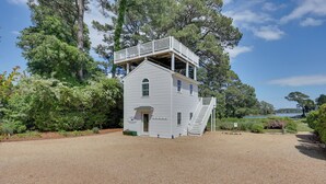 A two-story house with a balcony, surrounded by trees and a gravel driveway.