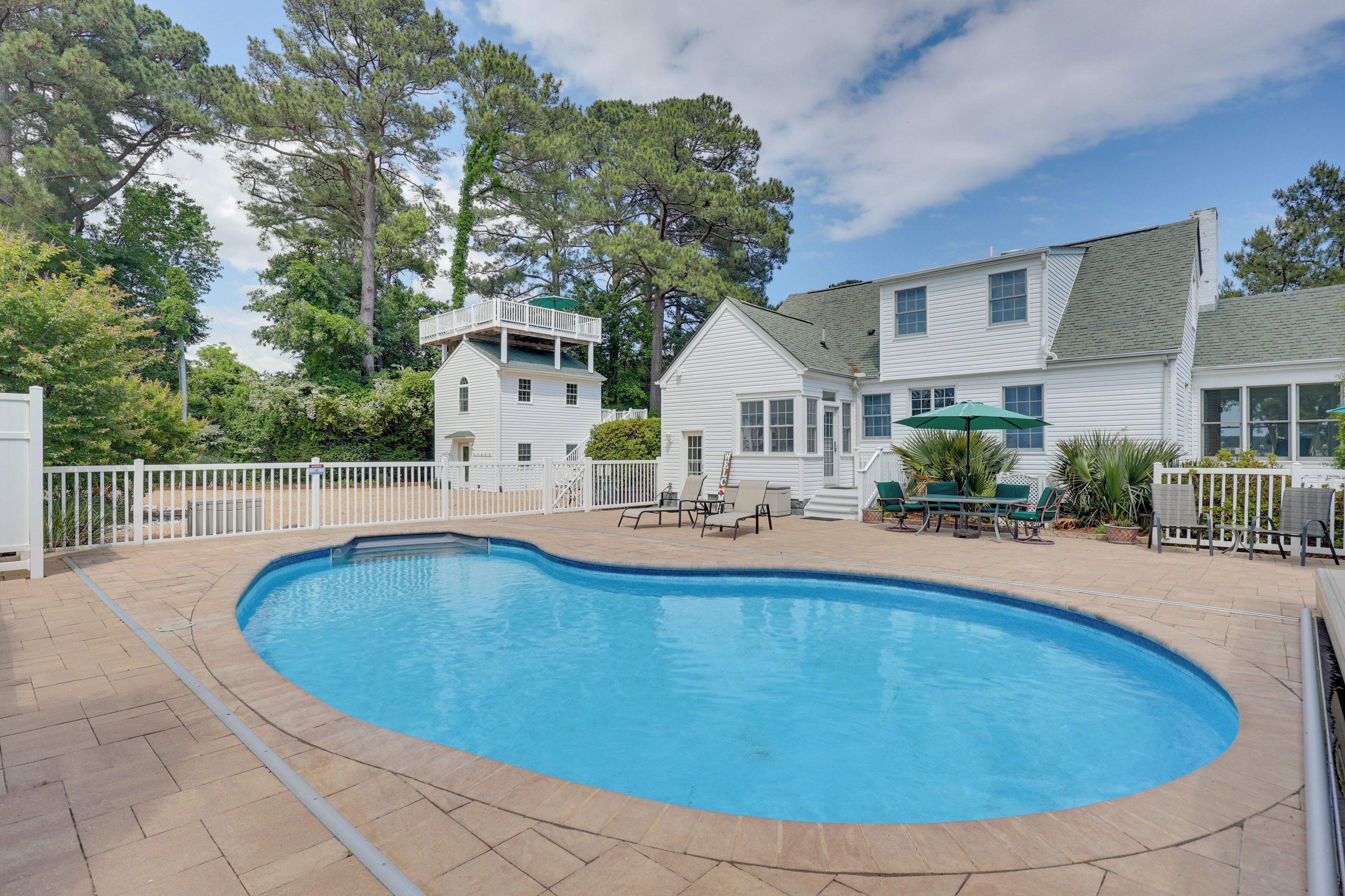 A swimming pool with a white fence, a covered patio area, and a two-story house with a balcony.