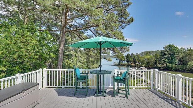 A deck with a table and chairs, a green umbrella, and a white railing.