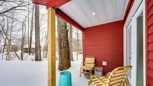 A covered porch with red siding, two striped chairs, a turquoise trash can, and a large tree. - 6 Mi to Polar Caves! All-Season Getaway w/ Sauna (Plymouth)