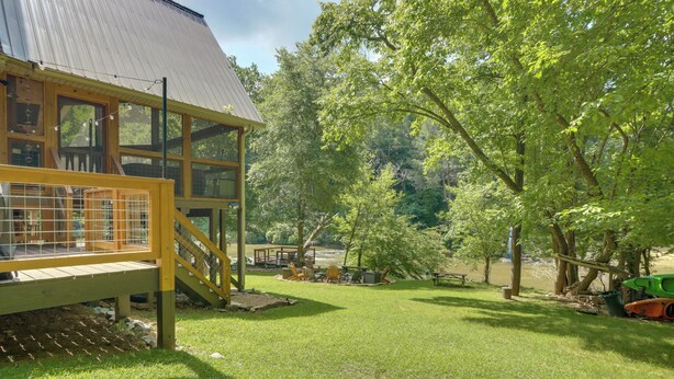 A wooden cabin with a deck, surrounded by a grassy yard and trees. - Riverfront, Hot Tub! Coosawattee River Resort Home (Ellijay)