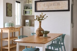 A dining area with a wooden table, teal chairs, a woven vase with flowers, and a framed sign above. - Riva Apt · Lake View - Finestra sul Lago (Navene)