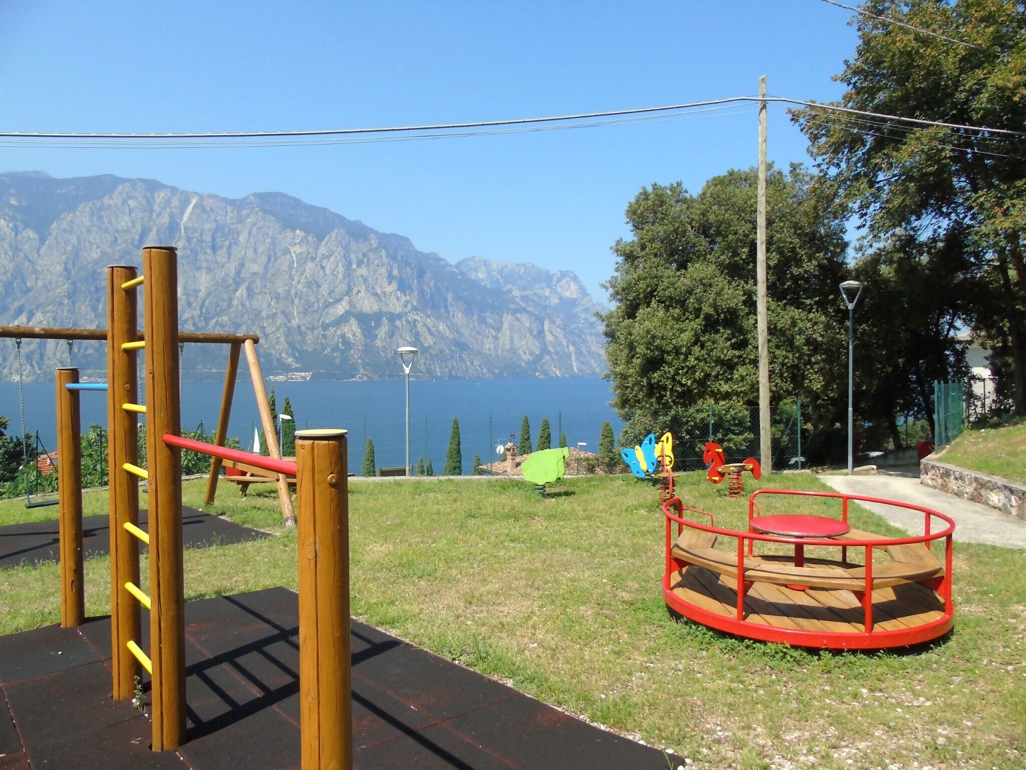 Un parque infantil con columpios y un carrusel, con montañas y un lago al fondo.