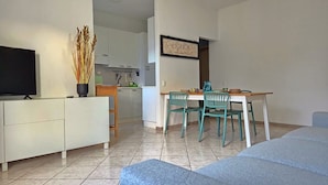 Ein modernes Wohnzimmer mit Fernseher, einem Essbereich mit Stühlen und einer Küche im Hintergrund, sowie einem gerahmten Schild an der Wand.