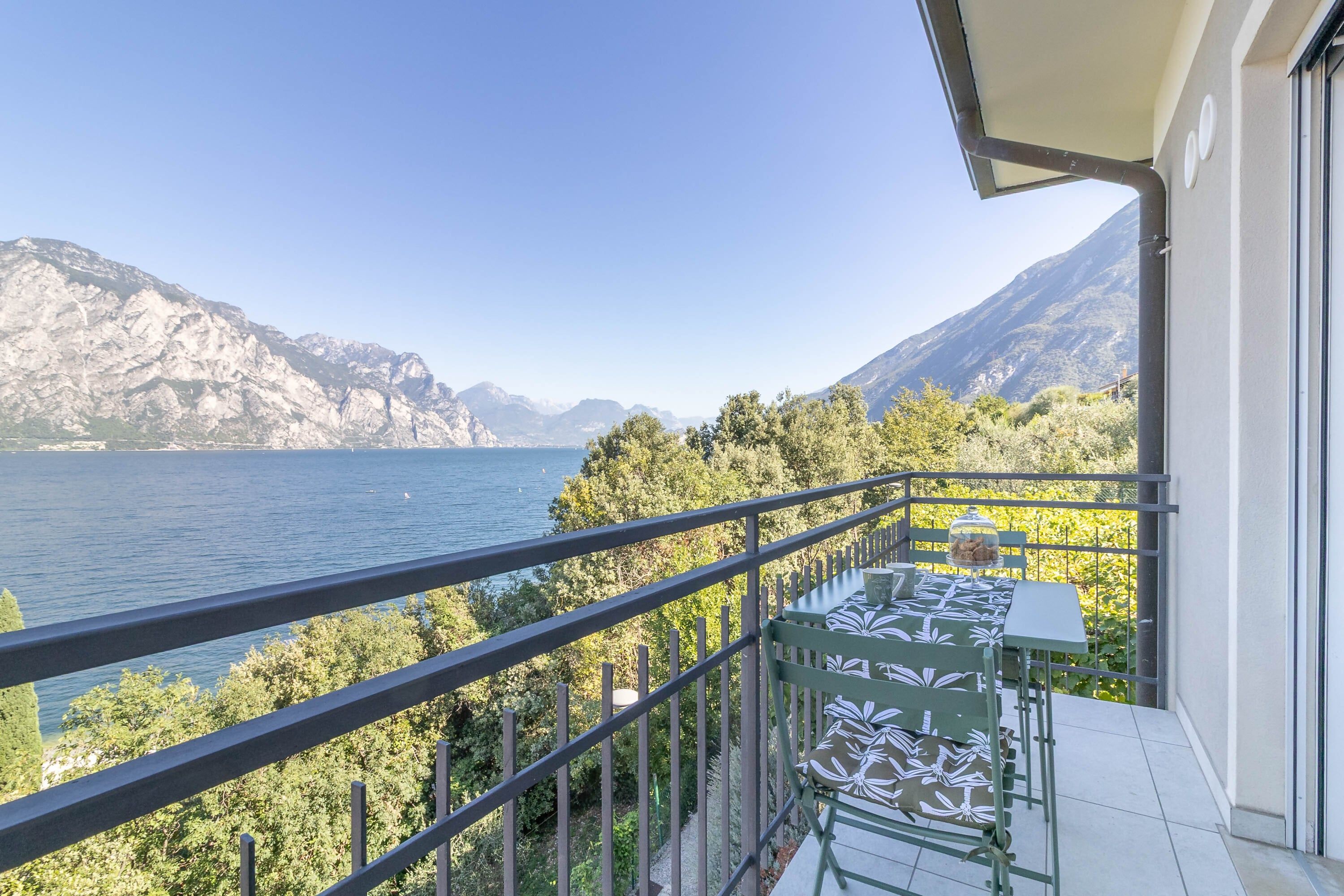 A balcony with a table and chairs overlooking a lake and mountains.