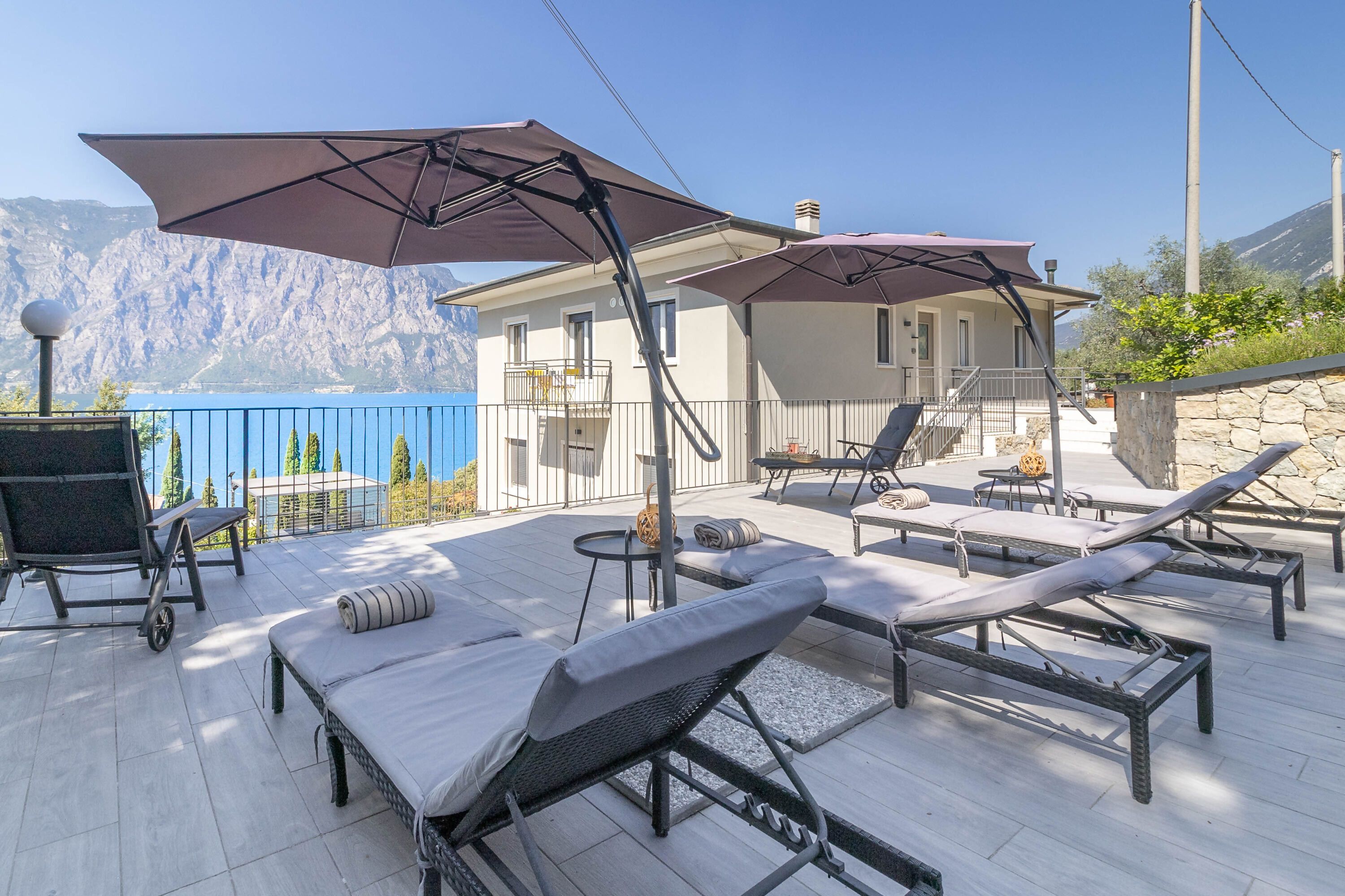 A terrace with sun loungers, umbrellas, and a view of mountains.